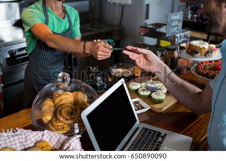 Staff giving credit card to customer at counter in coffee shop