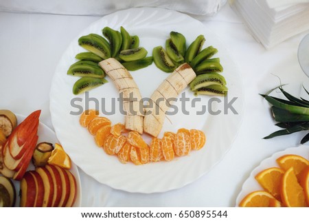 Bananas, kiwis and mandarines make a picture of palms on white plate