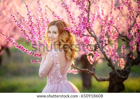 Beautiful woman in a long pink dress, in the garden of blooming peaches