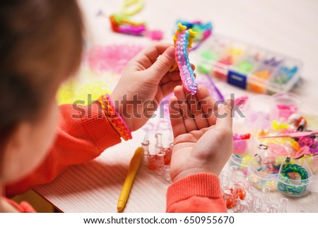 extracurricular activities, group, education and handwork concept - colored rubber bands for weaving accessories in the hands of a girl on a wooden background