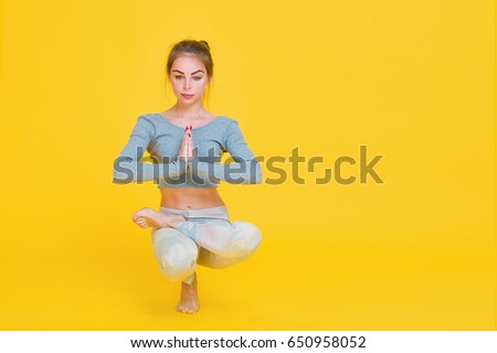 Young fit woman gymnast one leg balance pose isolated on yellow background