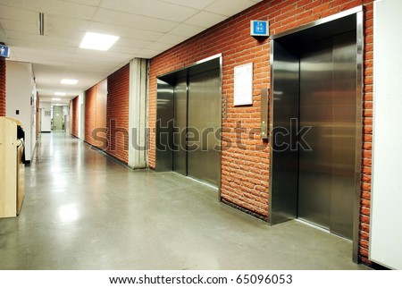 Freight and regular steel door elevators with signs in an empty hallway of modern building. Can be office, school, hospital.