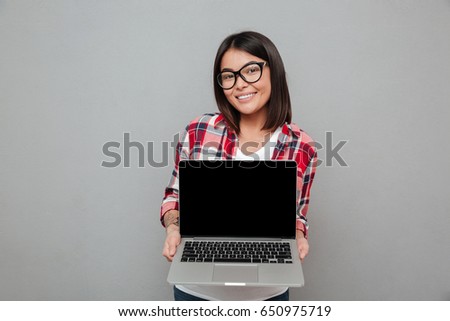 Image of happy young asian woman standing isolated over grey wall showing display of laptop computer.