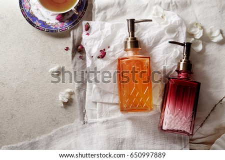 Horizontal mockup with two bottles of liquid soap with orange and cherry flavor on linen fabric with white shel, tea cup and rose petals. Rustic concept, copy space 