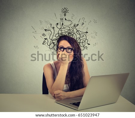 Young woman with thoughtful expression sitting at a desk with laptop with lines arrows and symbols coming out of her head Royalty-Free Stock Photo #651023947