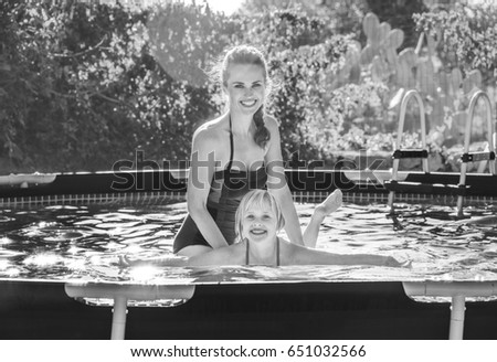 Fun weekend alfresco. happy active mother teaching daughter to swim in swimwear in the swimming pool