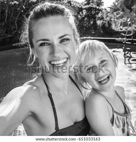 Fun weekend alfresco. happy active mother and child in beachwear in the swimming pool taking selfie