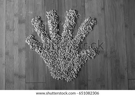 Black and white picture of a hand made from sunflower seeds on bamboo floor.
