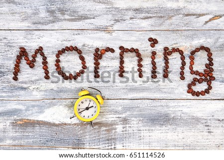 Inscription morning on wooden surface. Alarm clock and coffee grain.