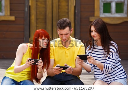 Group of three friends play mobile video game outdoors. Gamer excitement, face expression.