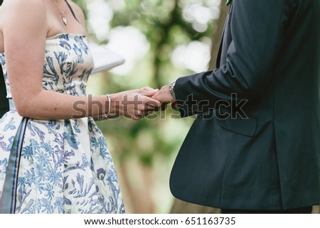 Bride in modern floral dress holding grooms hand during wedding 