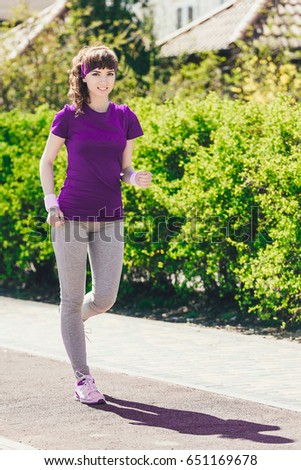 girl in sport on the nature.A young woman in a blue T-shirt runs against the background of green thickets. The concept of sport and healthy lifestyle
