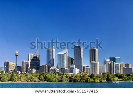 Sydney city central business district skyline over Royal botanic garden across blue waters of harbour under blue clean sky.