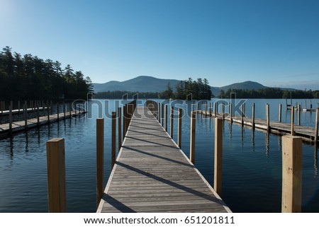 Wooden boat dock servicing blue clear-water Lake George during a calm and quiet early blue sky cloudless morning.