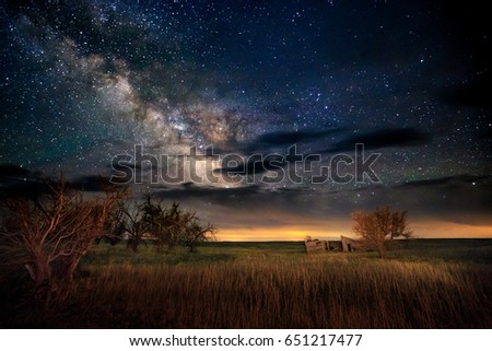 Long exposure night photo of the Milky Way in a rural setting. The Milky Way is very visible and the foreground is also lit up.