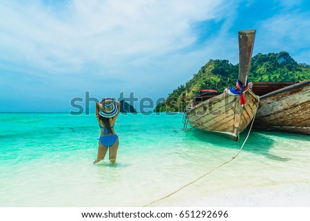 Happy woman in bikini and big hat standing with wooden boat on clear green sea water, Tub island, Andaman sea, Krabi province, Thailand