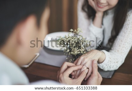 Close up pic of a young man's hand holding a sliver diamond engagement ring for the proposal to a young woman