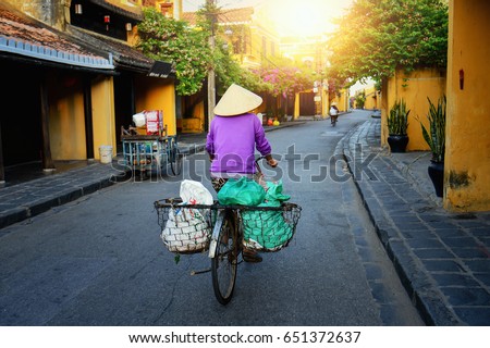 Vietnam people,Vietnamese ride bicycle on during sunrise,woman with Vietnam culture traditional,Morning view of busy street in Hoi An, Hoi An is the World's Cultural heritage site ,Hoi an, Vietnam Royalty-Free Stock Photo #651372637