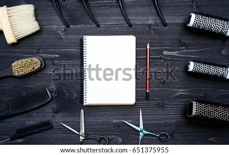 Hairdresser tools on wooden background. Blank card with barber tools flat lay. Top view on wooden table with scissors, hairbrushes and comb with empty notebook and pencil, free space