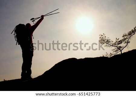 Silhouette of happy tourist with poles in hand above head. Sunny daybreak in mountains. Hiker with sporty backpack stand on rocky view point above misty valley.  Vivid and strong vignetting effect.. 