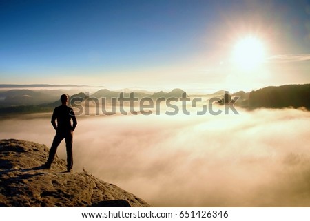 Man stands on rock above valley within daybreak and watch to hot Sun. Beautiful moment the miracle of nature. Feel free