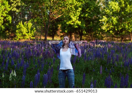 Beautiful slender young woman (girl) against the background of a clearing with purple flowers. The concept of hanging out in the summer in nature. Portrait on the hip. Daylight, outdoor shooting