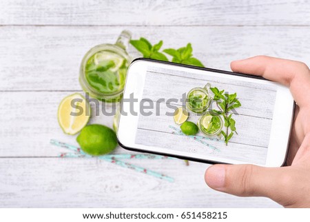 Hands taking photo lime and mint detox water with smartphone.