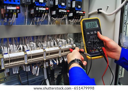 engineer tests the industrial electrical circuits with a multimeter in the control terminal box. Engineer's hands with a multimeter close-up against background of terminal rows of automation panel. Royalty-Free Stock Photo #651479998