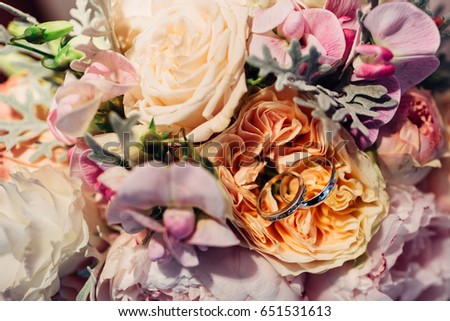 Wedding rings lie on the bouquet made of orange and pink peonies