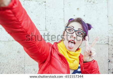 Fashion hipster woman with colorful hair taking selfie over wall background