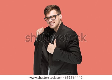 Young handsome man in black suit and glasses isolated on red background