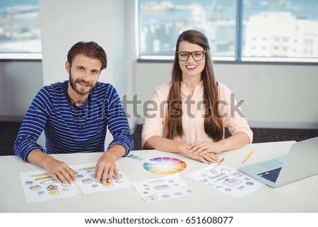 Portrait of smiling graphic designers sitting at desk in office