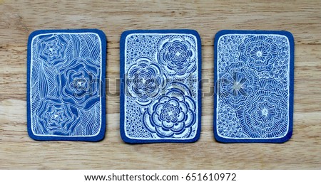Three card ATS drawn with white pen on blue background with floral motifs lying on wooden surface. Doodling. Zentangle