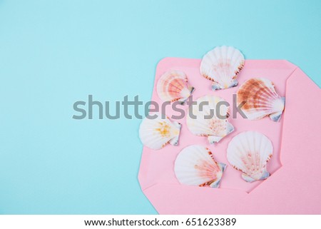 Pink envelope with scallop shells on colored mint blue background. Summer minimalistic card. Top view. Sea flat lay.