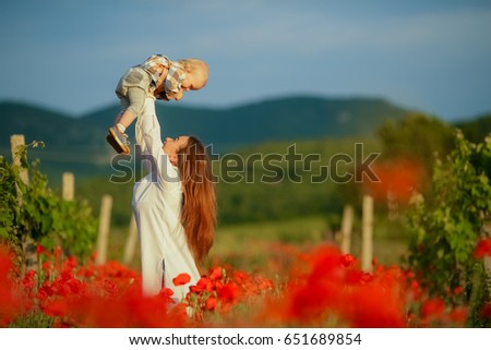 Happy motherhood, mother and baby playing in the field of poppies