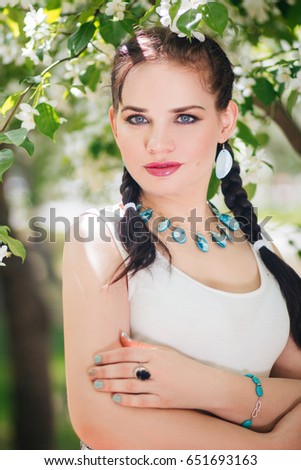 A beautiful girl in a flower garden in a white dress and big ornaments. Delicate portraits. Juicy photos. Blossoming apple-trees. Girl with pigtails. Sunny weather