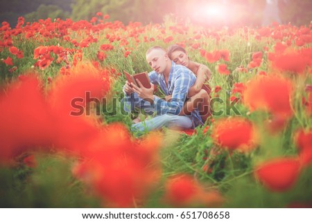 Happy couple breathing fresh air in a colorful field with red poppy flowers. young amazing couple kissing among red flowers. Happy family concept. Love story. Fashion. Summertime. Sunny day. Romantic.