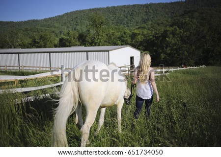 Young Woman with Blonde Hair Walking with a Horse