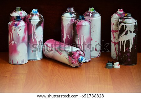 Still life with a large number of used colorful spray cans of aerosol paint lying on the treated wooden surface in the artist's graffiti workshop. Dirty and stained cans for spray art