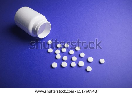 White medical pills on a colored background with a vial