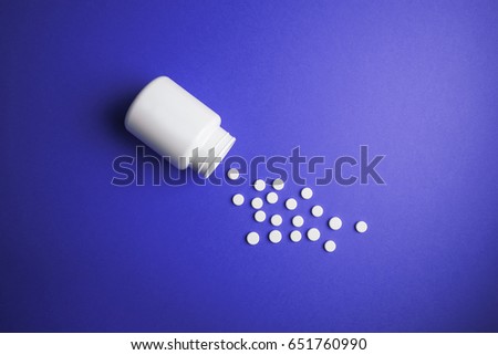 White medical pills on a colored background with a vial