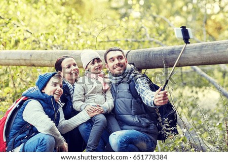 travel, tourism, hike, technology and people concept - happy family with backpacks taking picture by smartphone and selfie stick in woods