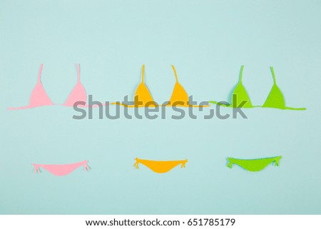 Three colorful paper bikini swimsuits on mint blue background. Minimalistic summer flat lay with negative space. Beach concept. 