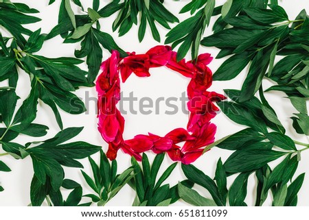 Wreath of pink petals with space for text. Peonies petals and green leaves.
