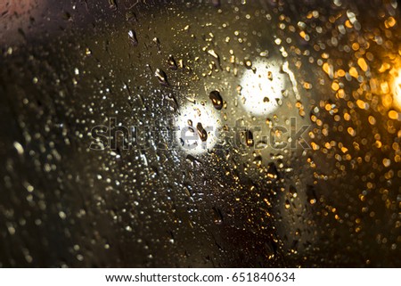 water drops on the windscreen front of the car, abstract picture in a rainy day with traffic jam in the night on urban road.