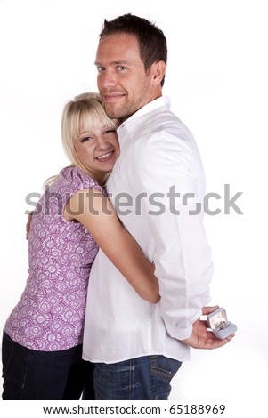 A couple cuddling and showing their love by holding each other with a smile.  He is holding a wedding ring behind his back.  Getting ready to pop the question.