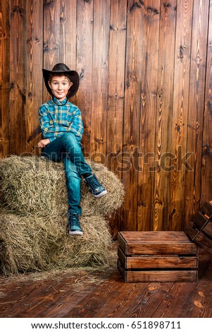 Portrait of a cute nine year old boy posing near the hay on the background of wooden wall. Western style, cowboy. Kid's fashion. Clothes for children.