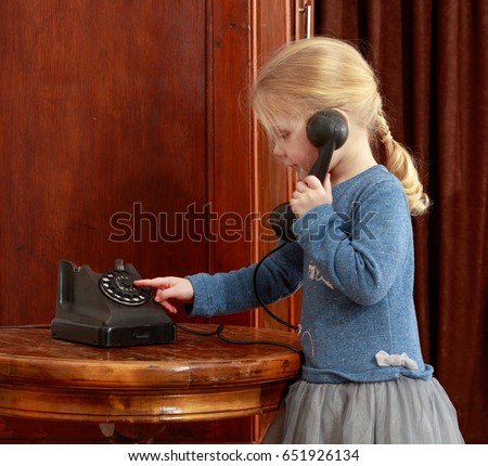 The little girl in the interior of the fifties of the last century keeps the ear-hook of vintage phone. The girl calls her grandmother.