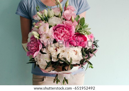 Woman in blue t-shirt holding a bouquet of pink and white peonies on a turquoise background
