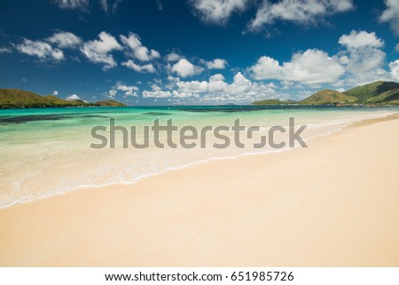 Scenic view on the Indian ocean with sandy beach, blue sky with white clouds, green palm trees and granit rocks in Seychelles